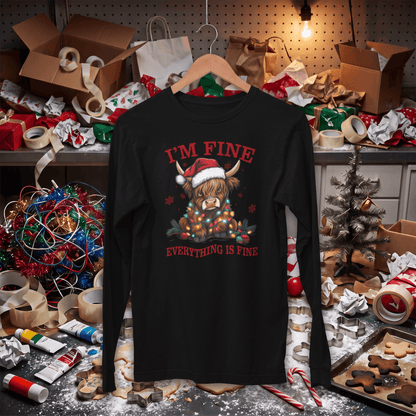A black long-sleeve t-shirt with a Christmas graphic of a Highland cow wearing a Santa hat, surrounded by ornaments and the text 'I'M FINE' and 'EVERYTHING IS FINE' in red. The shirt is displayed on a wooden hanger against a cluttered, festive holiday workshop background.
