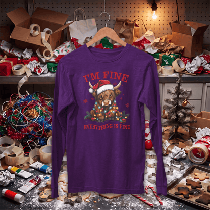 A purple long-sleeve t-shirt with a cartoon Highland cow graphic and the text 'I'M FINE' and 'EVERYTHING IS FINE' in red, hanging on a wooden hanger in a messy Christmas-themed room.