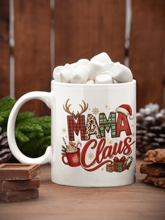 A white ceramic mug filled with marshmallows, decorated with a festive 'Mama Claus' holiday graphic, set on a wooden surface with chocolate and pinecones.