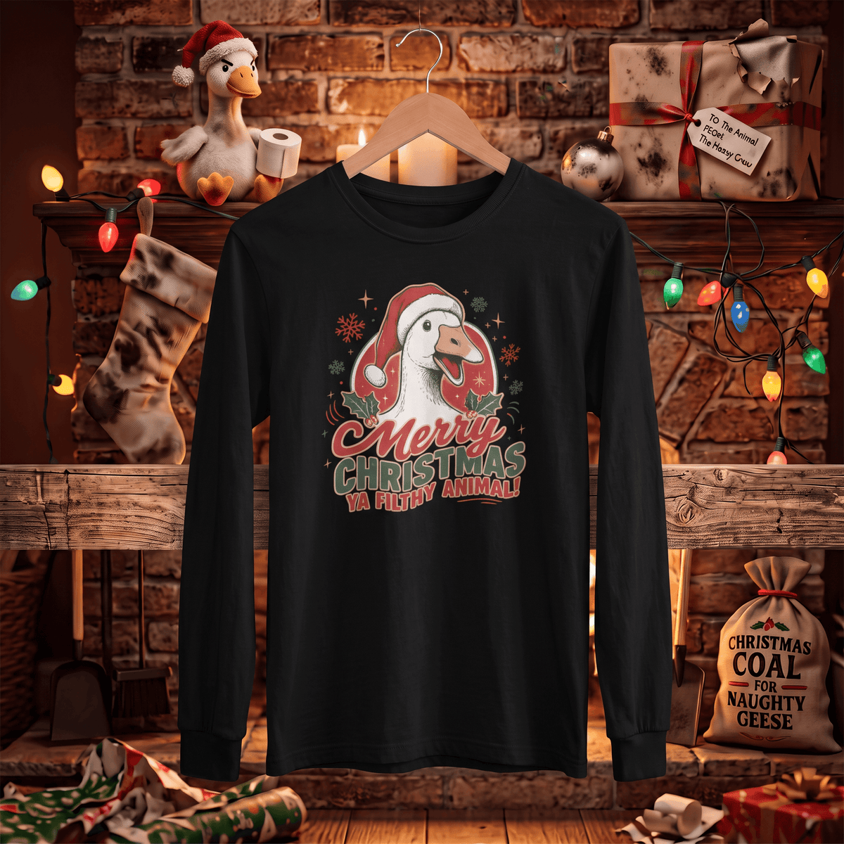 A black long-sleeve t-shirt with a Christmas goose graphic hanging on a wooden hanger. The graphic features a white goose in a red Santa hat with the text 'Merry Christmas Ya Pretty Animal!'.