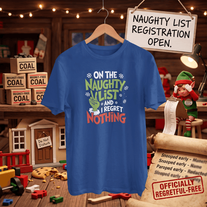 A blue graphic t-shirt hanging on a wooden hanger in a Christmas-themed room setting. The shirt features a festive graphic with the text 'ON THE NAUGHTY LIST AND I REGRET NOTHING' in green, white, and red lettering, accompanied by a green stocking and snowflake details.