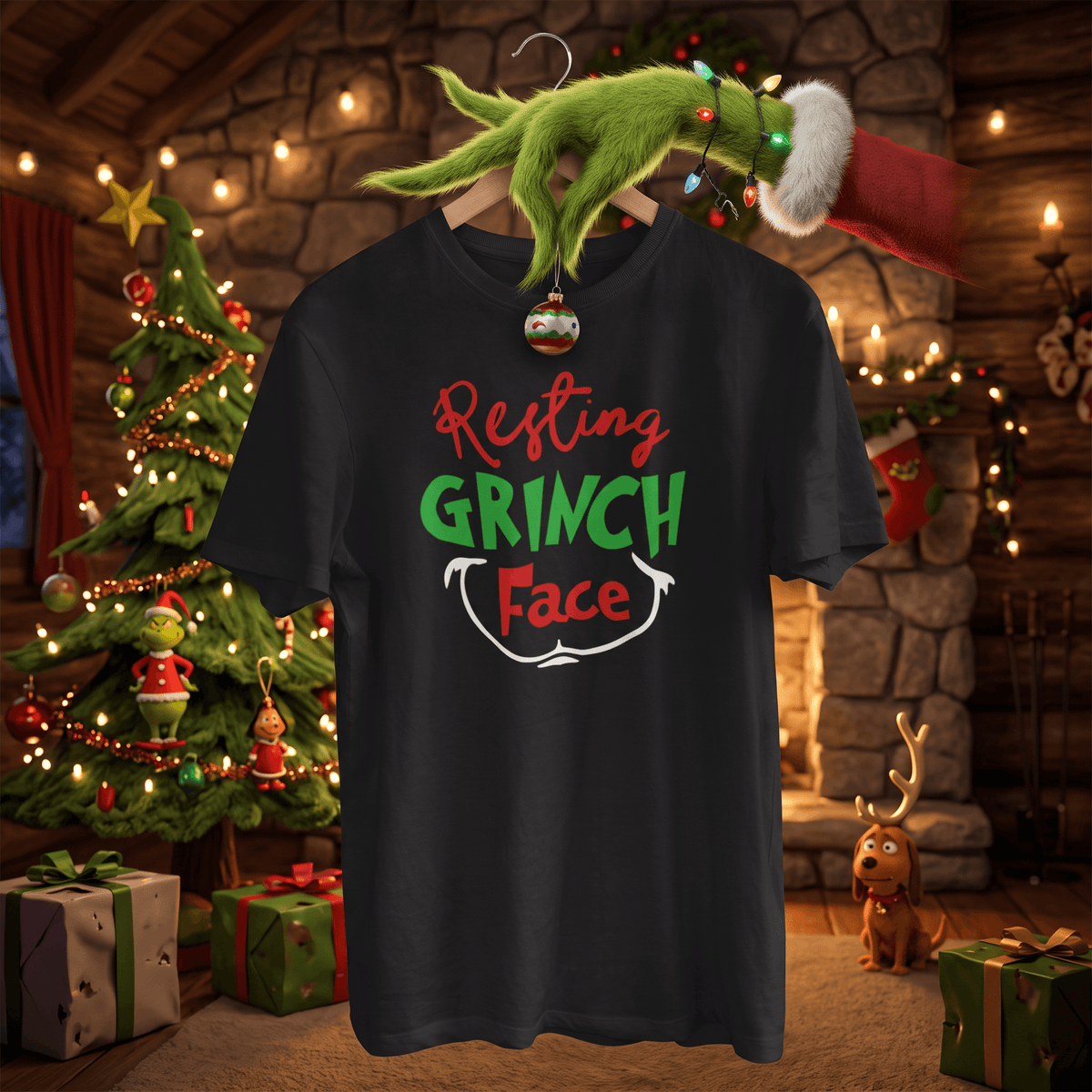 A black graphic t-shirt featuring the text 'Resting GRINCH Face' in red, green, and white. The shirt is shown hanging on a wooden hanger decorated with a green Grinch hand, Christmas lights, and a Santa hat, set against a cozy, warmly lit Christmas living room background with a tree, fireplace, and gifts.