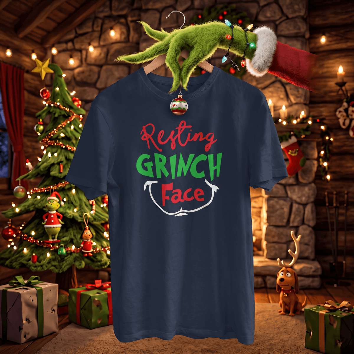 A navy blue graphic t-shirt featuring the text 'Resting GRINCH Face' in red, green, and white. The shirt is displayed on a hanger decorated with a Christmas ornament, surrounded by a festive Christmas tree, stockings, and a fireplace in the background.