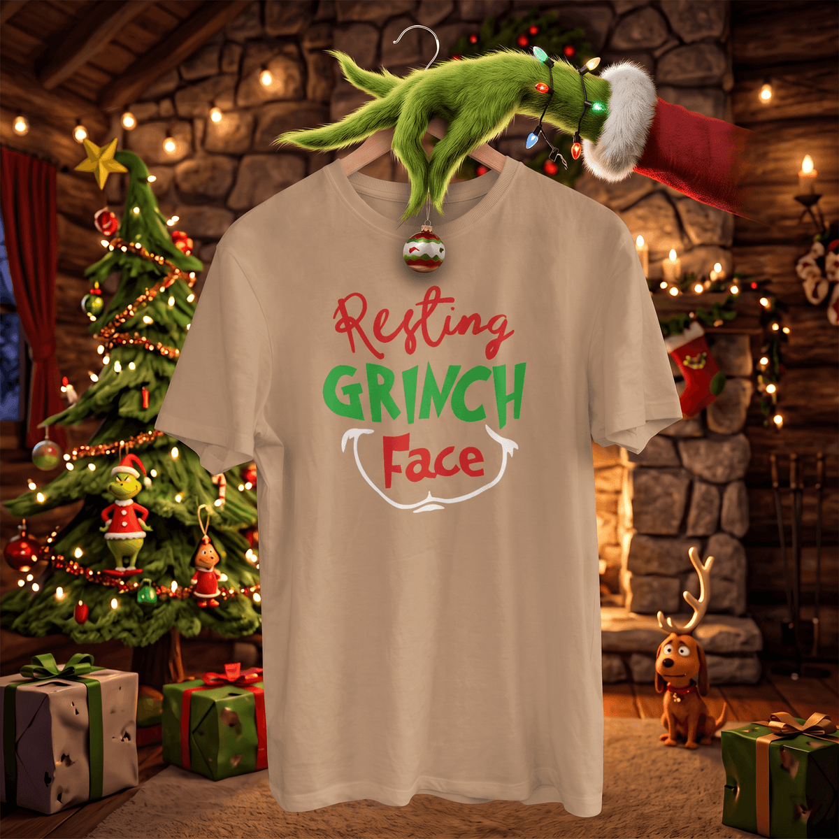 A beige graphic t-shirt featuring the text 'Resting GRINCH Face' in red, green, and white. The shirt is displayed on a hanger with a green Grinch hand and Santa hat hanging above it, set against a cozy Christmas log cabin background with a decorated tree and gifts.