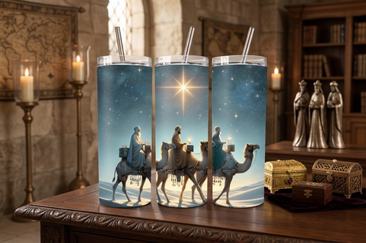Three tall clear plastic tumblers with clear straws, printed with a Christmas Nativity scene showing three camels, wise men, and the star of Bethlehem, displayed on a wooden table in a warmly lit room.